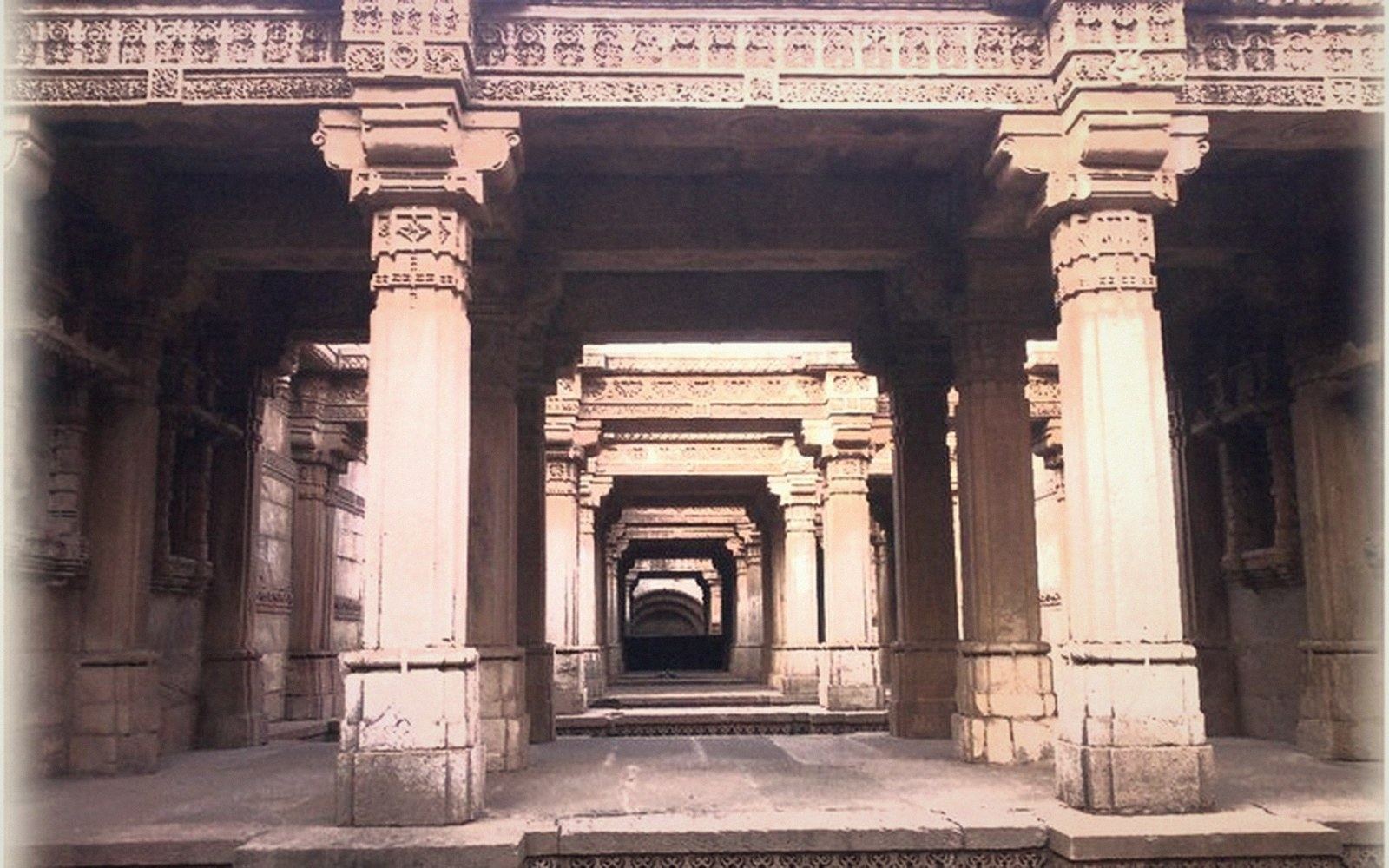 Rows of intricately carved sandstone pillars line a stepwell's descending corridor