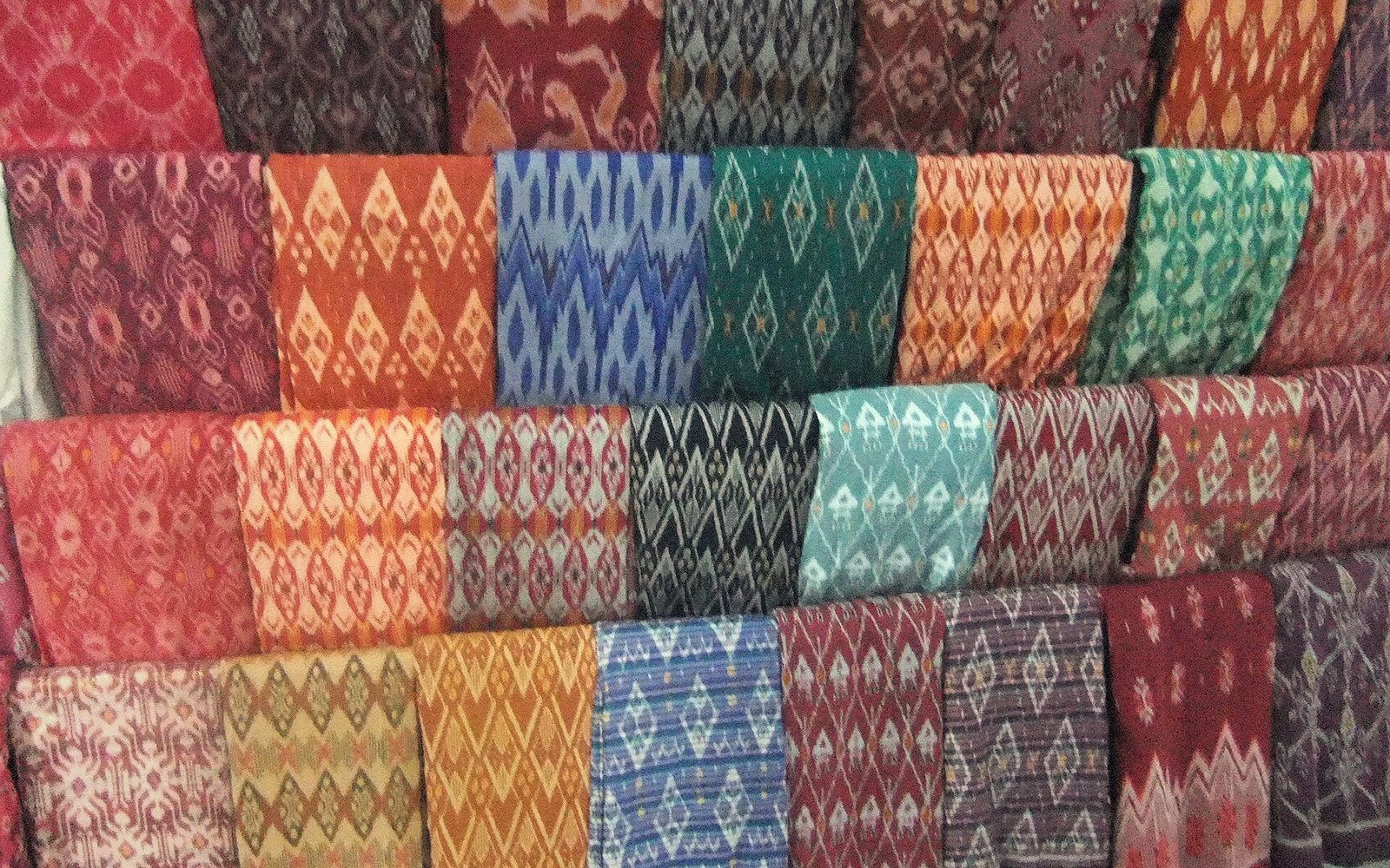Rows of colorful ikat-patterned fabrics displayed in stacked folds on a shelf